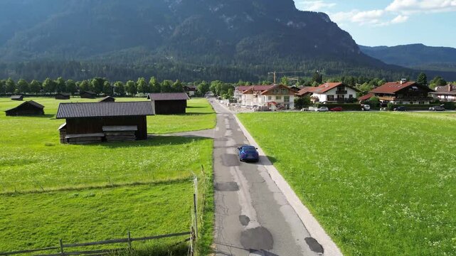luxury car driving in garmish partenkirchen germany bavaria local roads wooden huts village mountain background sunny sunshine