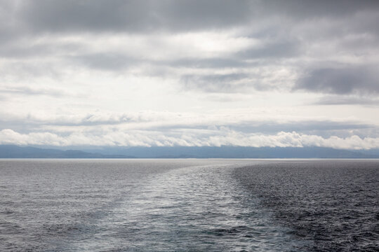 View of the entrances to Loch Hourn and Loch Nevis from the back of a ferry in the Atlantic on a cloudy morning, Image shows the Scottish mainland hills covered in cloud and calm waters with a wake