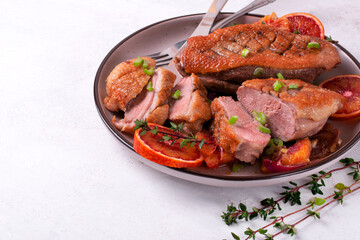 Roasted duck breast with blood oranges, thyme and onion served on the ceramic plate on the white table. Copy space