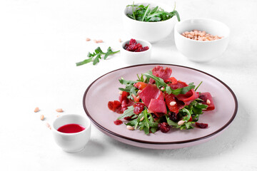 Salad with smoked duck breast, arugula, dried cranberry and pine nuts on the ceramic plate. Exquisite cold appetizer