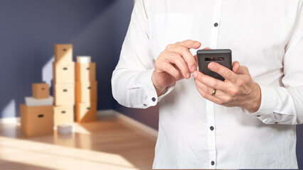 Mobile phone in hands of businessman. Cropped man near moving boxes. Businessman is relocating to new office. Guy is looking for place to move through phone. Person calls movers for moving