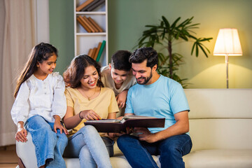 Happy Indian family of four relaxing on a sofa, reading books Or viewing photo album together