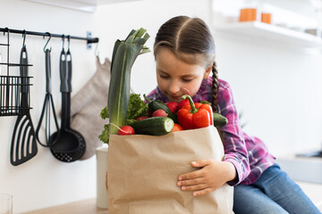 Young girl holding grocery bag filled with fresh vegetables in kitchen. Healthy lifestyle, home cooking, and nutrition concept. Child exploring fresh produce.