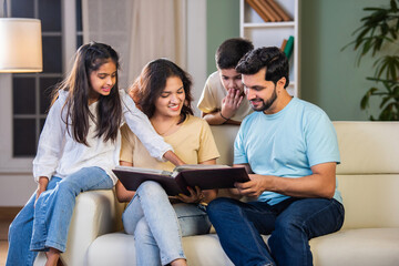 Happy Indian family of four relaxing on a sofa, reading books Or viewing photo album together