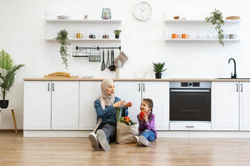 Family bonding in modern kitchen, sharing fresh vegetables and enjoying time together. Muslim mother and daughter prepare to cook healthy food at home.