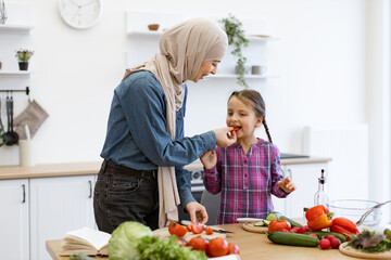 Concept of family, healthy eating, and togetherness. Muslim mother and daughter cutting ingredients for salad. Kitchen setting with fresh vegetables and bonding moment.