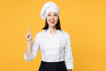 Young smart chef cook baker woman she wear white shirt black apron uniform toque chefs hat holding index finger up with great new idea isolated on plain yellow background studio. Cooking food concept.