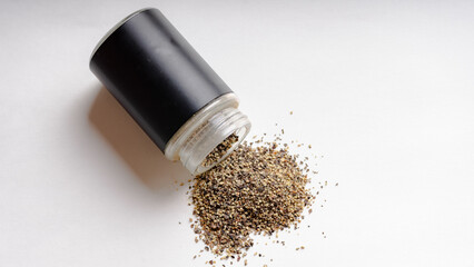 Grounded Black pepper spilling out of a pepper shaker on a white background