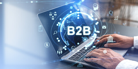 Businessman typing on a laptop with B2B icons and a digital globe overlay on a blue-toned background. Concept of business-to-business technology and networking