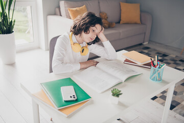 Photo of cute tired little boy schoolkid learning from home reading book apartment room interior indoors