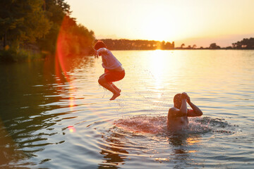 boy jumping into the water from his father's shoulders in a lake at sunset