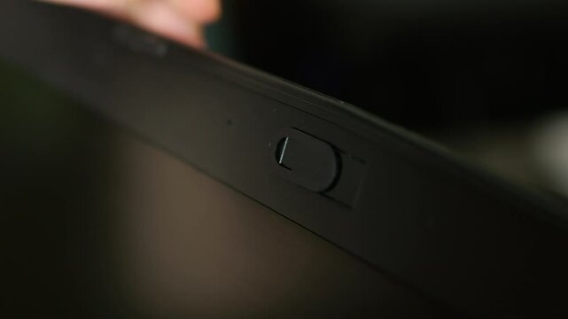 Female finger using closing webcam privacy cover slider shutter on black laptop.