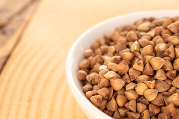 Raw buckwheat groats in a white ceramic dish on a wooden table, macro.