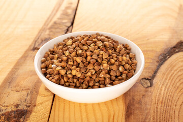 Raw buckwheat groats in a white ceramic dish on a wooden table, macro.