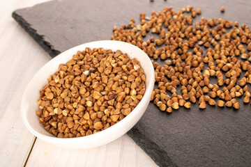Raw buckwheat groats in a white ceramic bowl on slate stone, macro.