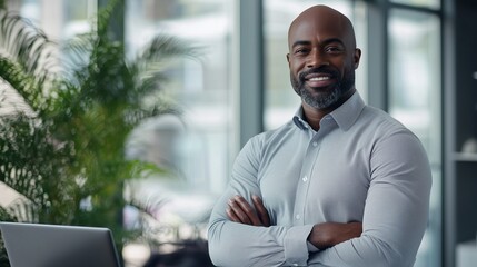 Naklejka premium Portrait of confident african-american businessman standing with laptop male office employee in smart casual wear looking at the camera and smiles leaned back at te desk ceo manager sturtup owner.