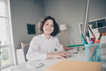 Photo of cute small clever schoolkid wearing white shirt learning from home apartment room interior...