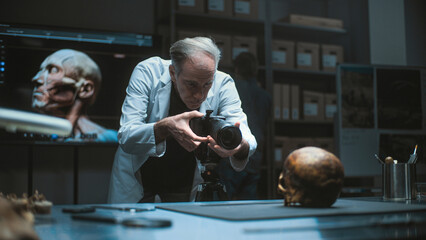 Senior archaeologist takes photo of fossil remains of prehistoric human skull with professional...