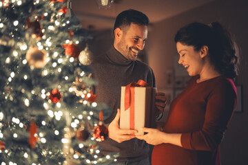 A loving happy husband surprising his beautiful wife with a gift on Christmas Eve