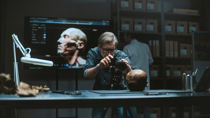 Mature archaeologist takes photo of fossil remains of prehistoric human skull in archaeological...