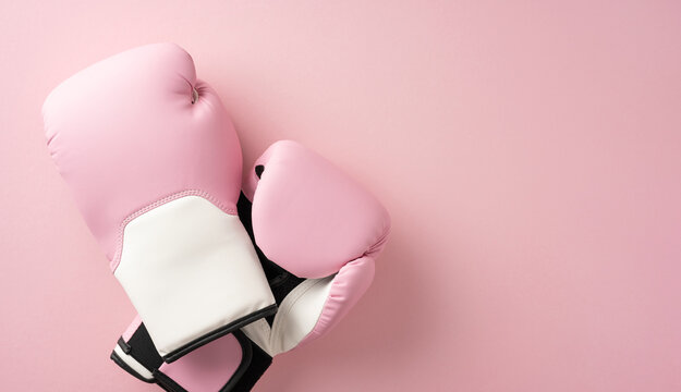 A pair of pink boxing gloves representing strength and empowerment in breast cancer awareness month against a pink background - Powered by Adobe