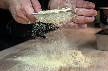 sieving flour at table against black background, close-up