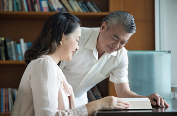 Mature Lovely Asian Couple, Middle aged man woman Enjoying a Shared Reading Experience in a Cozy Library