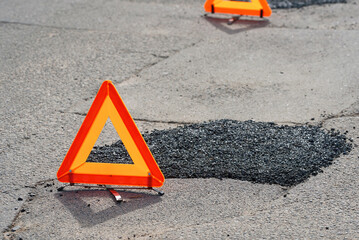 Fresh asphalt patch marked by warning triangle for safety. Roadwork. Patched asphalt road. Asphalt...
