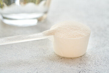 Collagen powder in a plastic measuring spoon with a glass of water