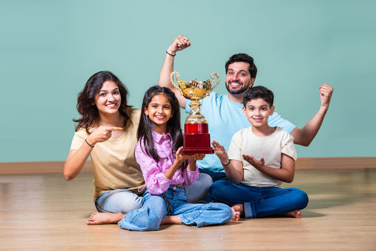 Indian boy or girl holding a trophy, celebrated by proud parents standing beside in a joyful moment