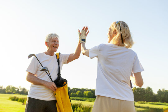 An elderly couple in sportswear exchange greetings on a golf course after a successful shot. Man and woman playing and succeeding together. Sunny day in the background 