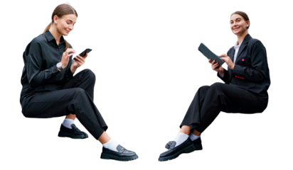 Two young professional women in black attire, sitting and engaging with technology, smiling confidently.