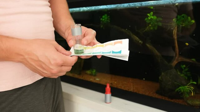 Man is comparing a water sample to a test strip, analyzing the water quality in his aquarium