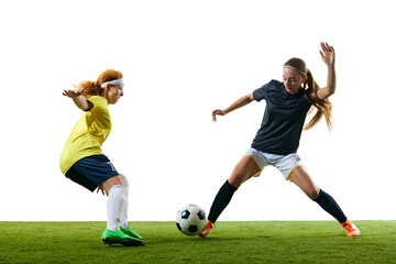 Two young, female soccer players in intense one-on-one moment, both poised to make critical move on green soccer field. Concept of sport, competition, tournament, games, event.
