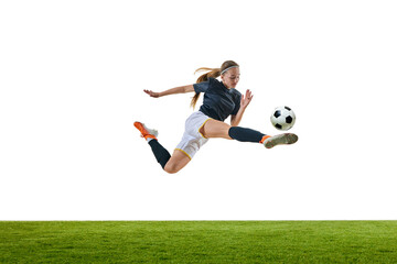 Young woman, soccer player, mid-flight, aiming precise kick at ball, showcasing agility and focus on green stadium against white studio background. Concept of sport, competition, tournament, game