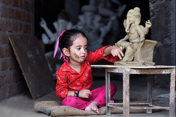 Asian Indian baby girl making eco-friendly Ganesh idol  for Ganesh Chaturthi celebration