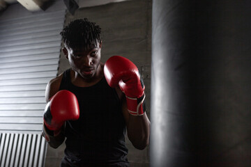 A powerful African American boxer in red gloves prepares for a punch in a gym, demonstrating...