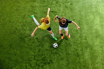 Dynamic soccer players, two young women chasing ball on vibrant green pitch, driven by competition...