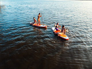 Aerial view of friends on sup board enjoying a day at lake during sunset.