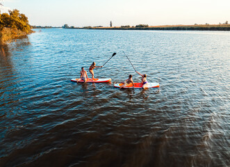 Aerial view of friends on sup board enjoying a day at lake during sunset.