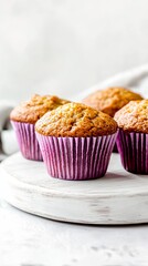 Close-up of three freshly baked muffins with a golden brown crust in purple paper liners on a white wooden board.