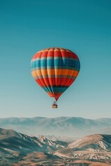 Obraz premium A colorful hot air balloon floats against a blue sky over a mountain range.