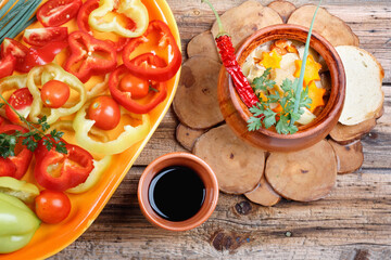 Traditional rustic home vegetable stew with raw vegetables, spices in clay pots with red  wine on old vintage wooden table.