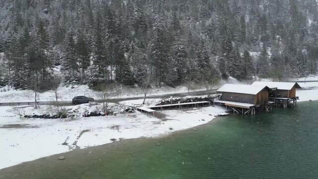 car parked next to mountain lake winter landscape snow covered snowing backwards aerial drone shot wooden huts white scenic water blue