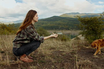 A woman in nature, kneeling with her dog on the shore of a tranquil mountain lake
