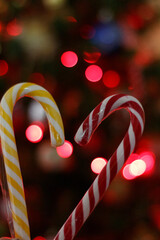 two candy canes, forming a heart shape with red bokeh lights in the background, symbolizing festive holiday spirit.