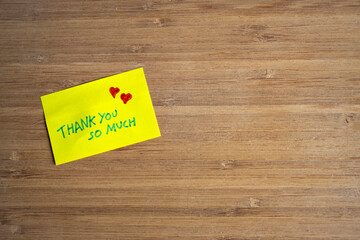 Vista superior de la nota adhesiva amarilla de agradecimiento con corazones sobre fondo de madera