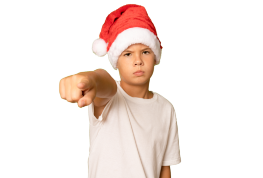 Portrait of a serious boy in a red hat and white t-shirt pointing finger to camera on a transparent background. A child in a Christmas hat of Santa Claus.