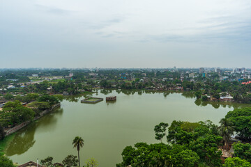 Fototapeta premium Aerial view of green cityscape with large lake, buildings surrounded by trees under cloudy sky.