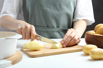 Woman cutting raw potato at white table, closeup